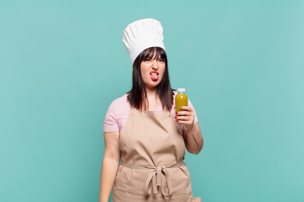 young chef woman feeling disgusted and irritated, sticking tongue out, disliking something nasty and yucky