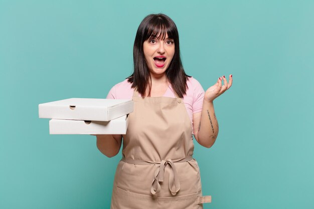 Young chef woman feeling happy, excited, surprised or shocked, smiling and astonished at something unbelievable