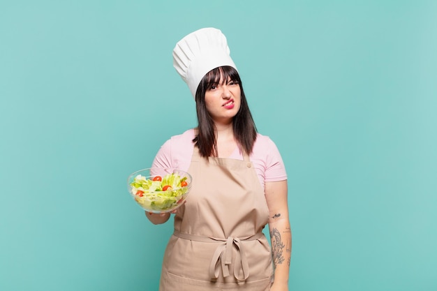 Young chef woman feeling puzzled and confused, with a dumb, stunned expression looking at something unexpected