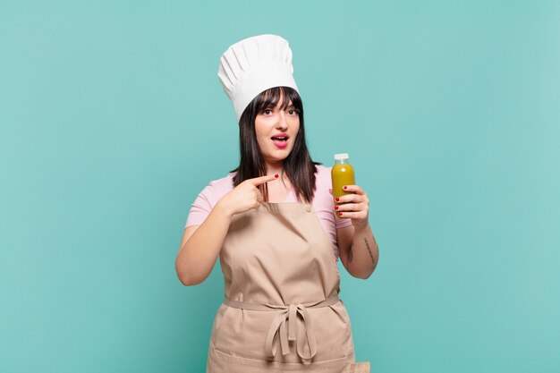 Young chef woman looking excited and surprised pointing to the side and upwards to copy space