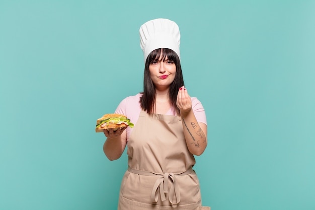 Young chef woman making capice or money gesture, telling you to pay your debts!