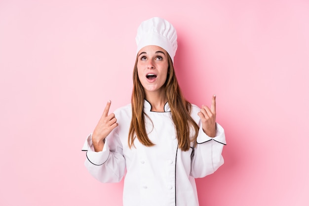 Young chef woman pointing upside with opened mouth.