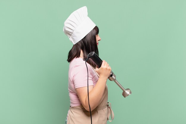 Foto giovane chef donna in vista di profilo che cerca di copiare lo spazio davanti a sé, pensando, immaginando o sognando ad occhi aperti