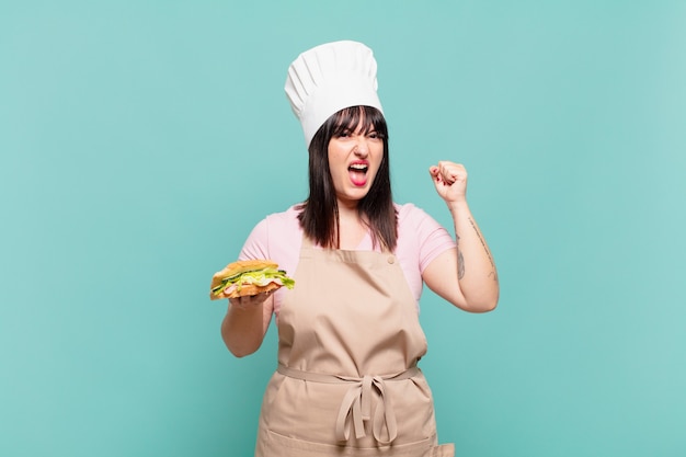 Young chef woman shouting aggressively with an angry expression or with fists clenched celebrating success