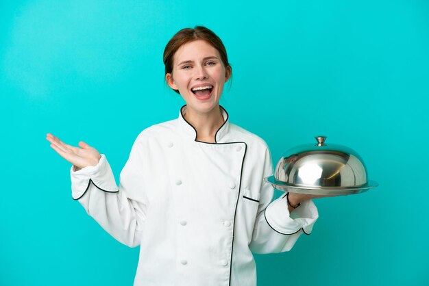 Young chef woman with tray isolated on blue background with shocked facial expression