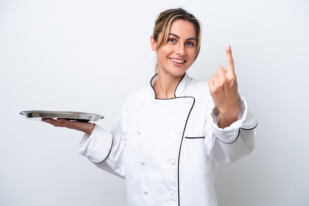 Молодая женщина-повар с подносом на белом фоне делает предстоящий жест