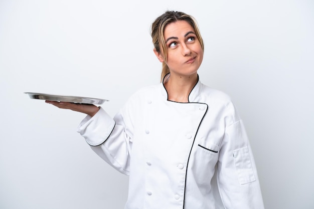 Young chef woman with tray isolated on white background and looking up