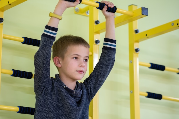 学校のスポーツジムの部屋の中の壁のはしごバーで運動する若い子少年。