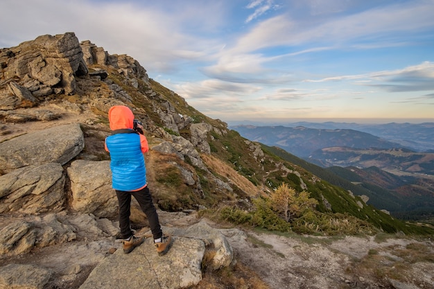 Young child boy hiker taking pictures in mountains enjoying view of amazing mountain landscape.