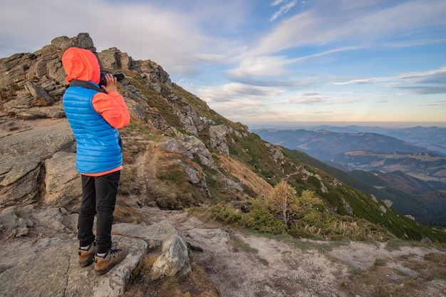 Young child boy hiker taking pictures in mountains enjoying view of amazing mountain landscape.