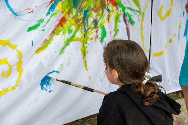 Photo young child creating a colourful abstract painting with a paintbrush on a sheet