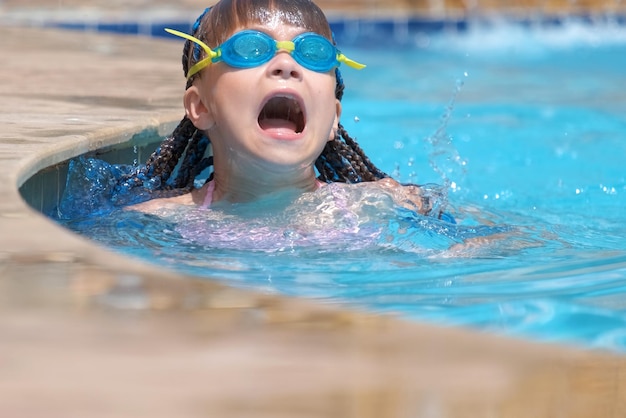 야외에서 푸른 수영장 물에서 수영을 배우는 고글을 쓴 어린 소녀 여름 레크리에이션 활동 개념