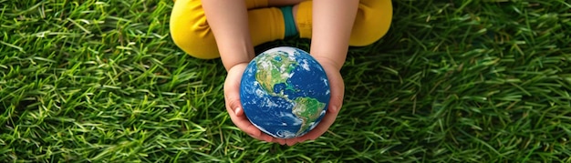 A young child holds a realistic Earth globe on a grass background shaped like a world map