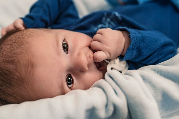 A young child is looking into the camera and sucking their hand