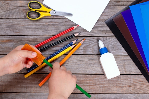 Photo young child sharpens pencils on wooden background