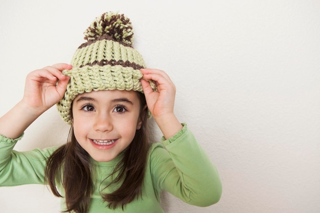 A young child with long brown hair, peering from underneath the brim of a knit hat