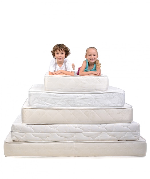 Young children sitting on lots of mattresses.