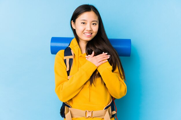 Young chinese backpacker woman isolated has friendly expression, pressing palm to chest. Love concept.