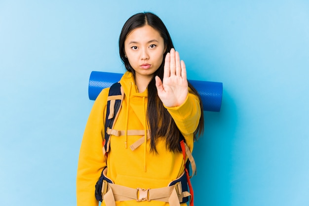 Young chinese backpacker woman isolated standing with outstretched hand showing stop sign, preventing you.