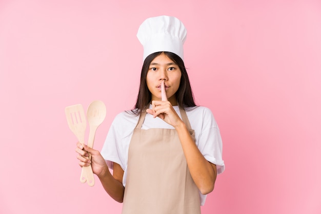 Young chinese chef woman isolated keeping a secret or asking for silence.