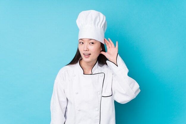 Young chinese chef woman isolated trying to listening a gossip.