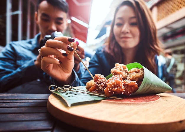 Giovani coppie cinesi che si siedono nel ristorante asiatico fuori. nella parte anteriore sul tavolo di legno c'è il cibo asiatico tradizionale - involucro di foglie di bambù. l'uomo sta guardando le immagini sulla fotocamera. ripresa widescreen.