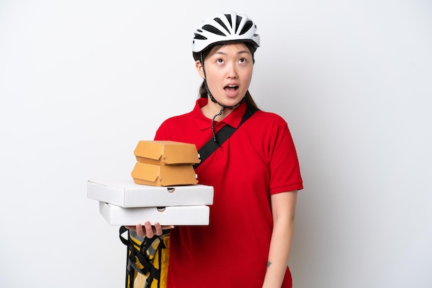 Young Chinese delivery woman taking takeaway food isolated on white background looking up and with surprised expression