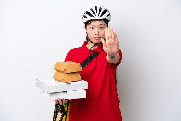 Young Chinese delivery woman taking takeaway food isolated on white background making stop gesture