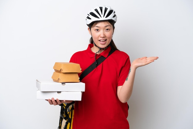 Young Chinese delivery woman taking takeaway food isolated on white background with shocked facial expression