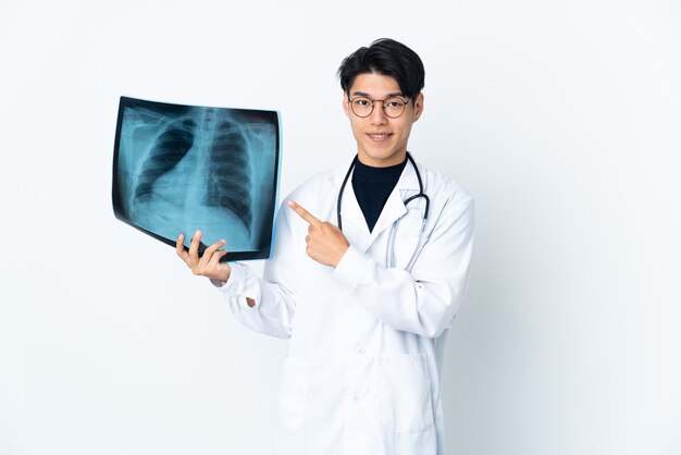 Young Chinese doctor man holding radiography isolated on white wall pointing to the side to present a product