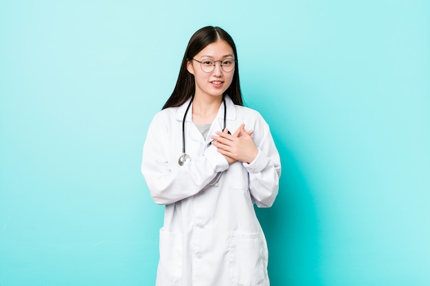 Young chinese doctor woman has friendly expression, pressing palm to chest. Love concept.