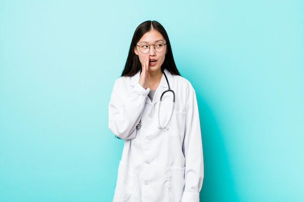 Young chinese doctor woman is saying a secret hot braking news and looking aside