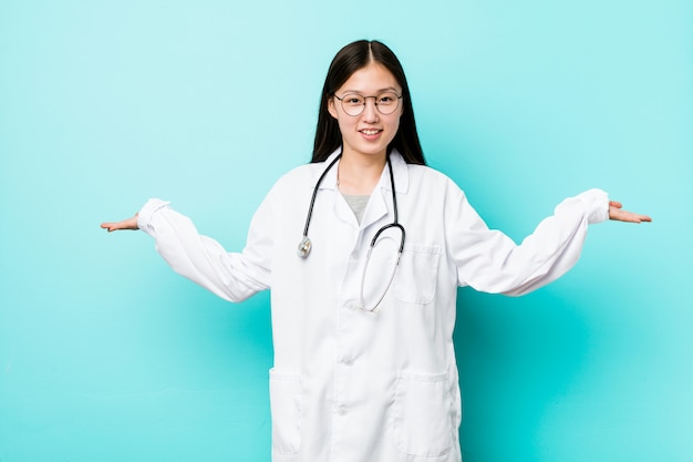 Young chinese doctor woman makes scale with arms, feels happy and confident.