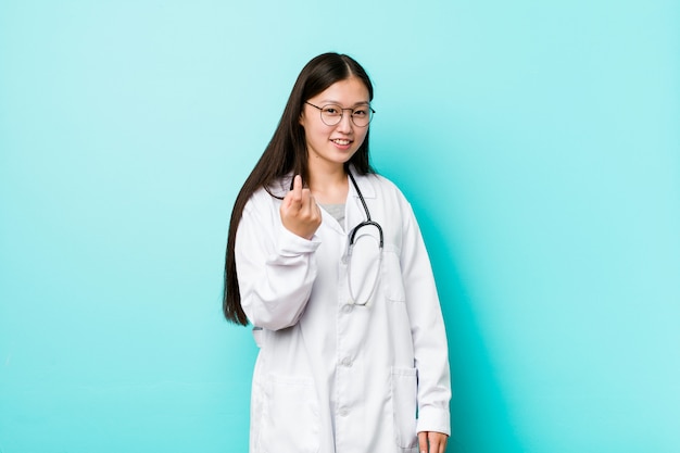 Young chinese doctor woman pointing with finger at you as if inviting come closer.