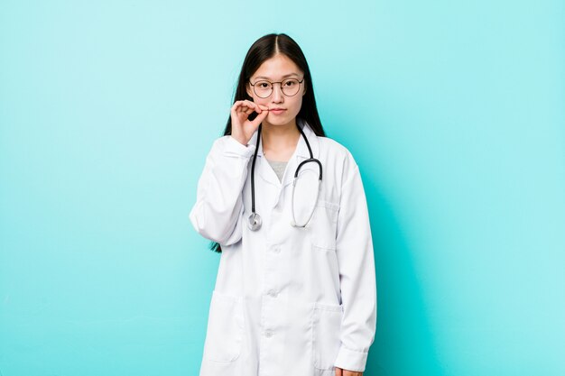 Young chinese doctor woman with fingers on lips keeping a secret.