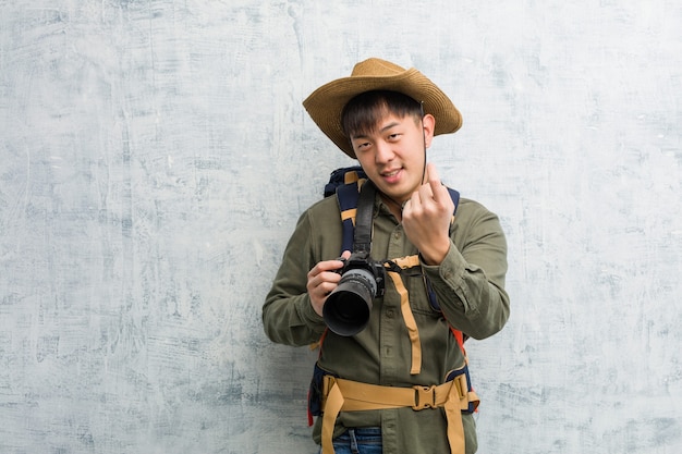 Young chinese explorer man holding a camera inviting to come