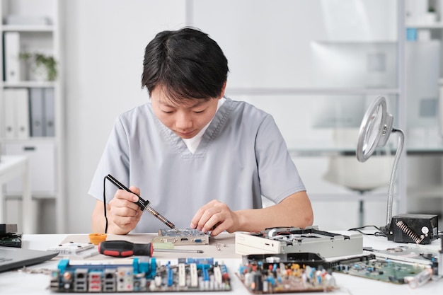 Young chinese female technician in uniform repairing circuit board