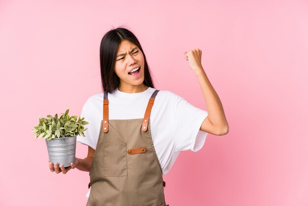 植物を保持している若い中国の庭師の女性は、勝利、勝者の概念の後拳を上げる分離しました。