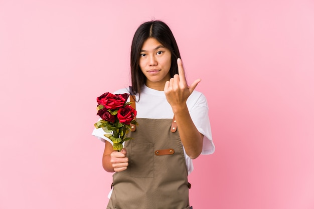 Young chinese gardener woman holding a roses isolated pointing with finger at you as if inviting come closer.