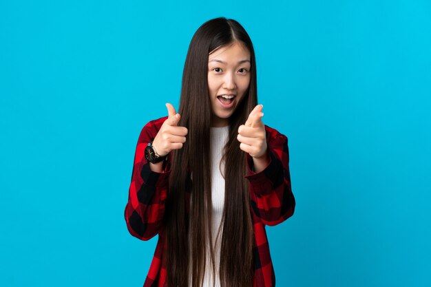 Young Chinese girl over blue surprised and pointing front