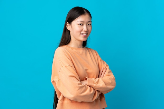 Young Chinese girl over blue with arms crossed and looking forward