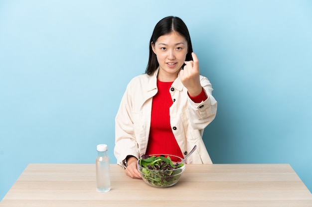 Young Chinese girl eating a salad doing coming gesture