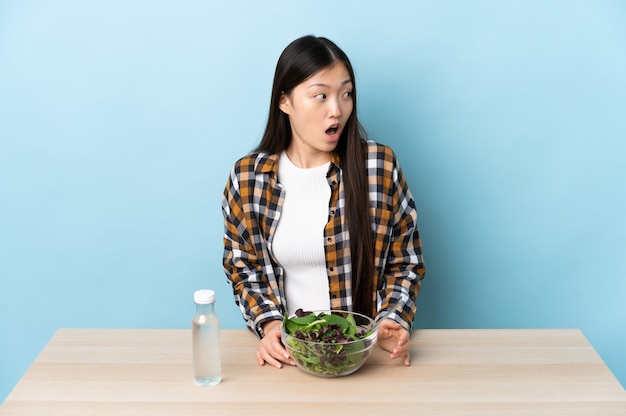 Giovane ragazza cinese che mangia un'insalata che fa gesto di sorpresa mentre guarda al lato