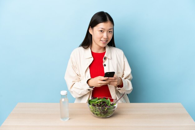 Young Chinese girl eating a salad sending a message with the mobile