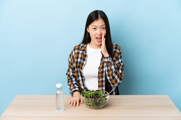Молодая китайская девушка ест салат и кричит с широко открытым ртом