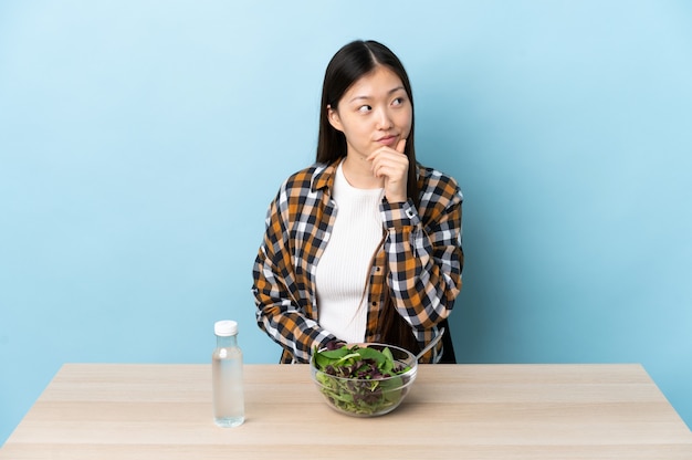 Giovane ragazza cinese che mangia un'insalata che pensa un'idea mentre osserva in su