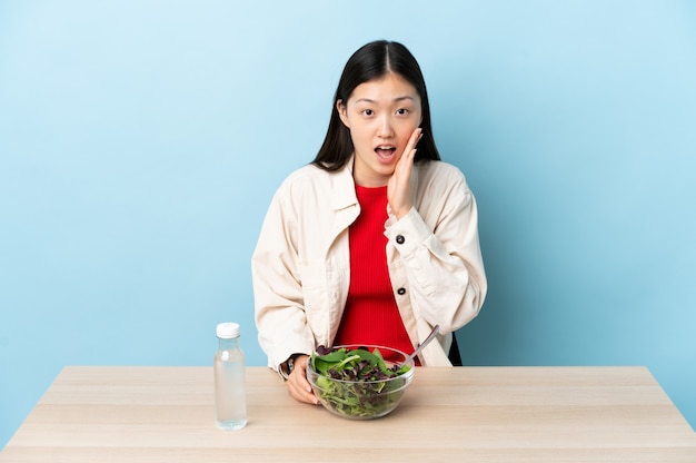 Young Chinese girl eating a salad with surprise and shocked facial expression