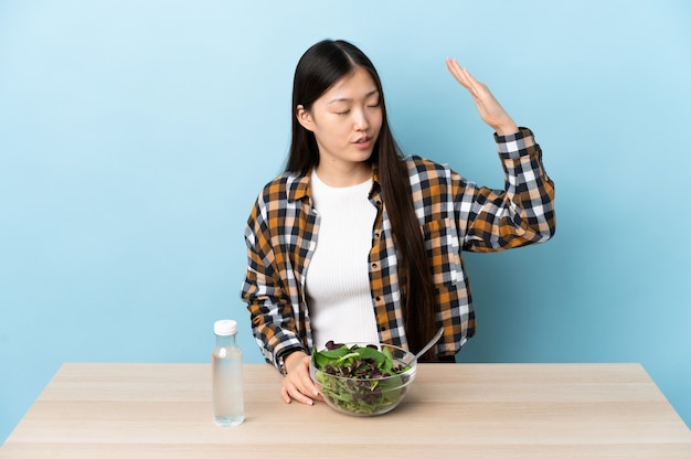 Young Chinese girl eating a salad with tired and sick expression