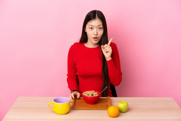 손가락을 들어 올리는 동안 솔루션을 실현하려는 테이블에서 아침을 먹고 젊은 중국 여자