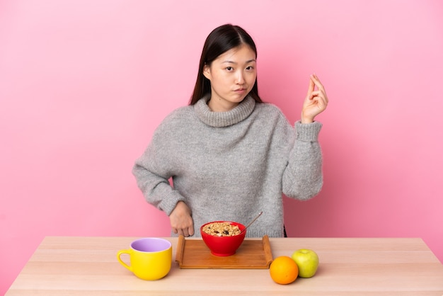 Giovane ragazza cinese che mangia prima colazione in una tabella che fa gesto italiano